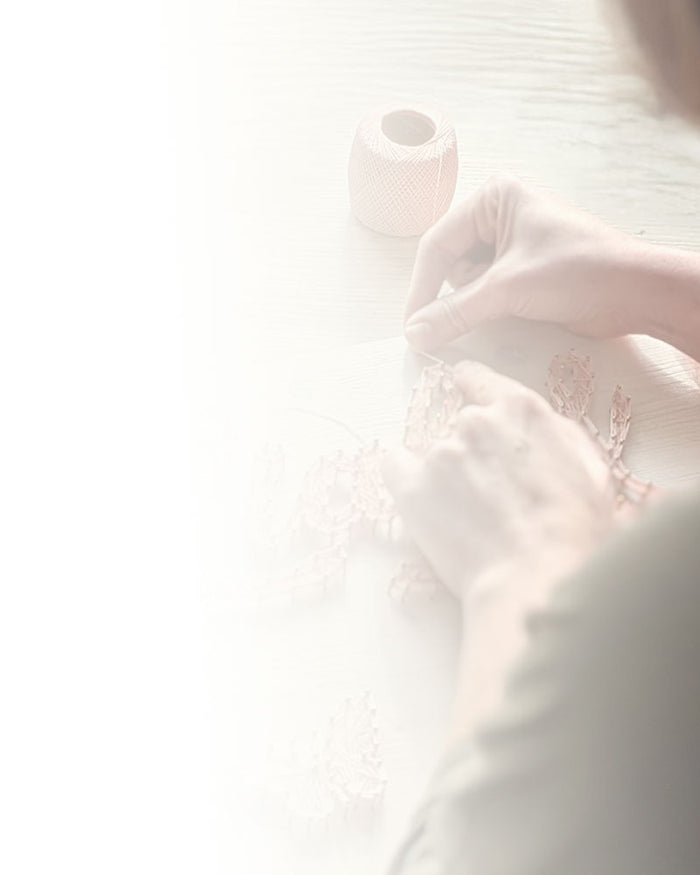 Person fädelt den Namen „Liah“ als Fadenbild in Altrosa auf ein helles Holzbrett.