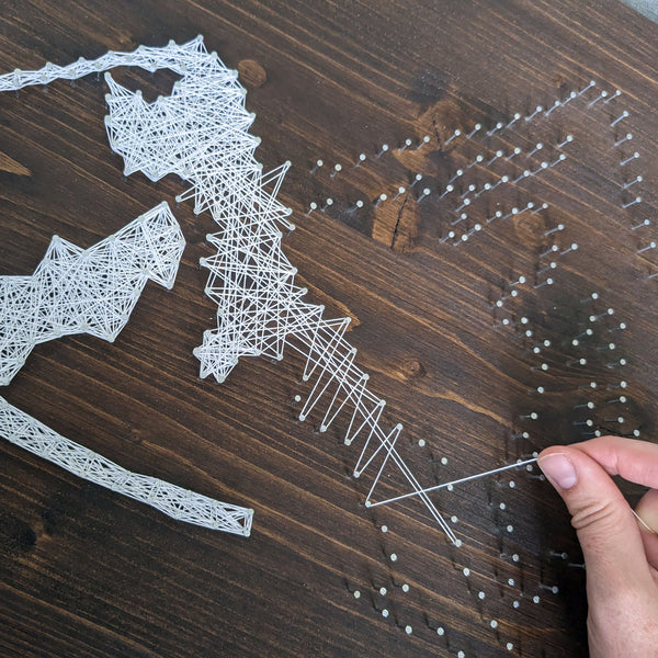 Hand fädelt Fadenbild aus weißem Faden auf dunklem Holz