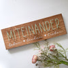 Fadenbild Schriftmotiv „Miteinander“ auf Holzbrett mit Blumen dekoriert