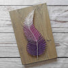 Fadenbild DIY-Set Feder auf grauem Holzbrett in Weiß und Lila als String Art